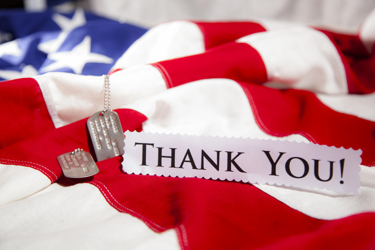 Military dog tags beside "Thank You" note. American flags. Patriotism.