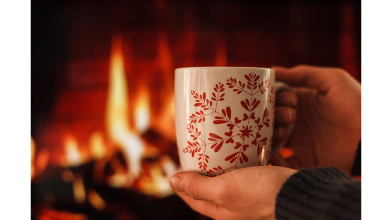 Hands holding a cup in front of a fireplace