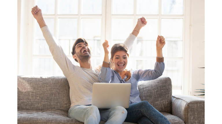 Happy young couple celebrate online victory, using laptop together