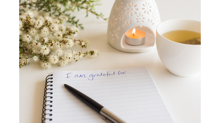 Close Up Of Handwritten Gratitude Text With Notebook, Pen, Cup Of Tea, Flowers And Oil Burner L