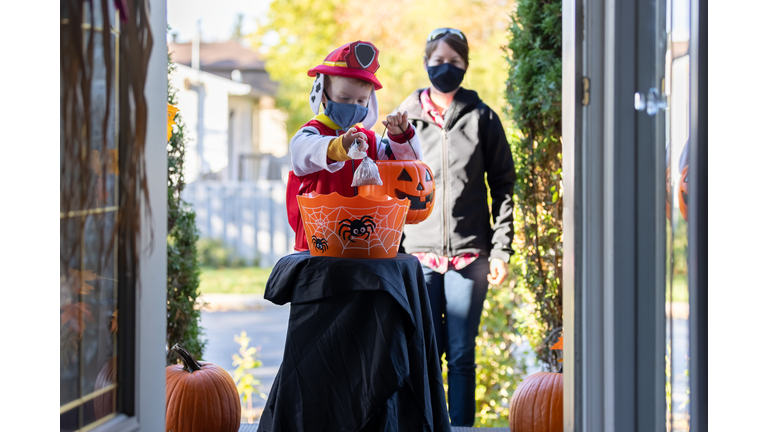 Young Boy wearing protective mask taking candies on Halloween at front door of a house