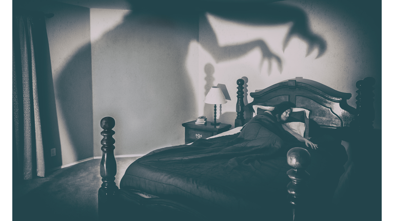 High Angle View Of Woman Sleeping On Bed With Spooky Shadow On Wall At Home