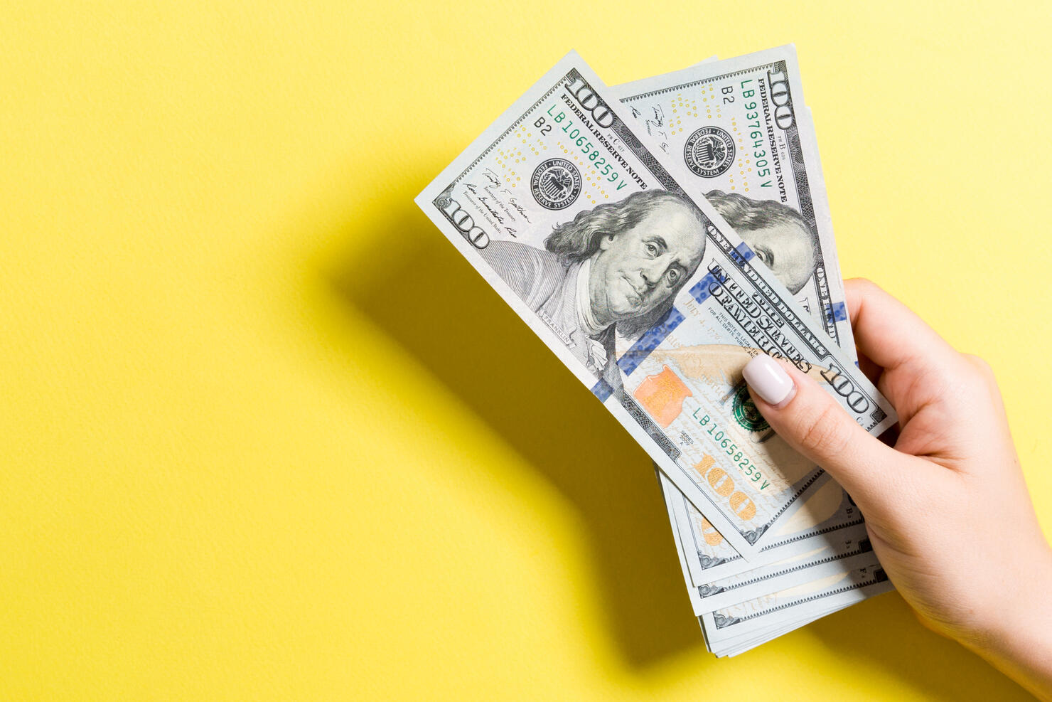 Female hand holding a bundle of money on colorful background. Top view of one hundred dollar banknotes. Salary concept with empty space for your design