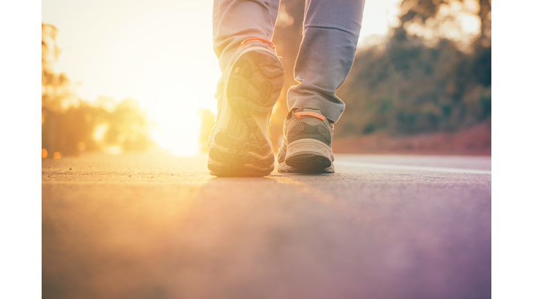 Low Section Of Man Walking On Road During Sunset