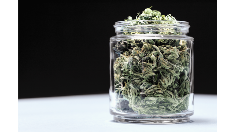 Marijuana leaves in glass jar on table against black background