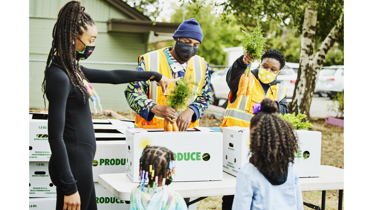 Volunteers showing family produce from CSA boxes at community center