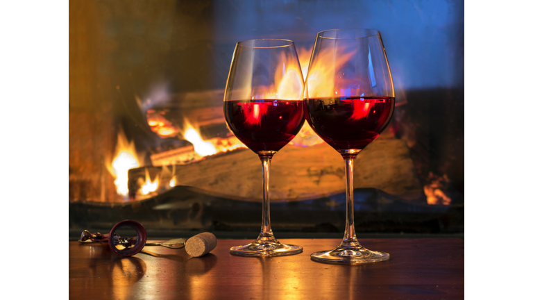 Two glasses of red wine in front of a fireplace