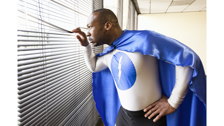 A black businessman office super hero looks out the window and checks his next business move.