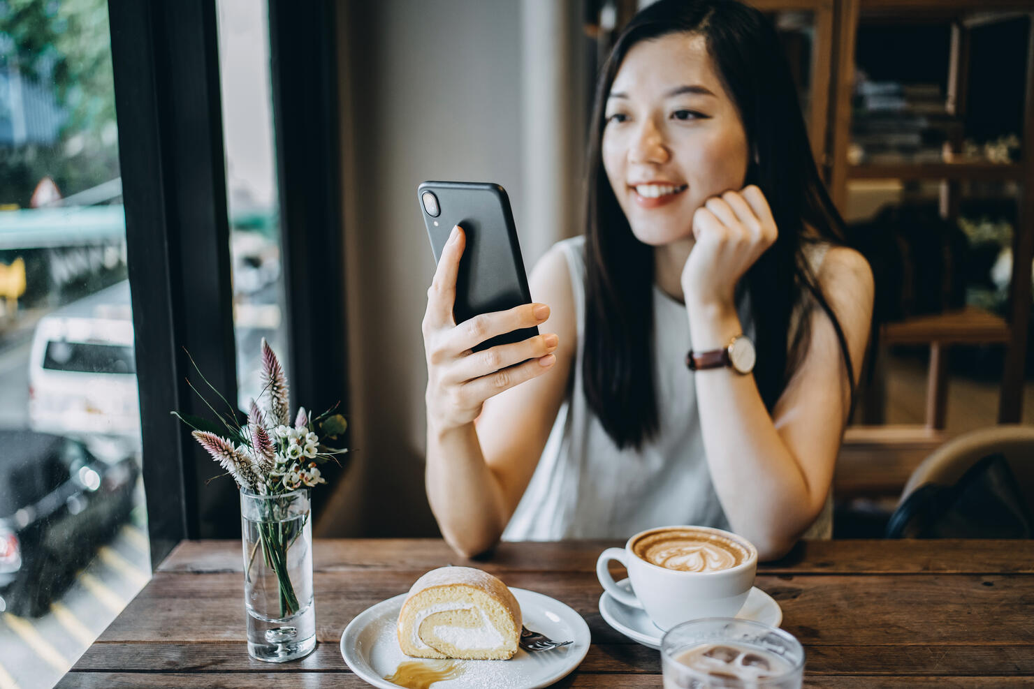 Smiling young woman using smartphone while having a relaxing time enjoying coffee and cake in a coffee shop