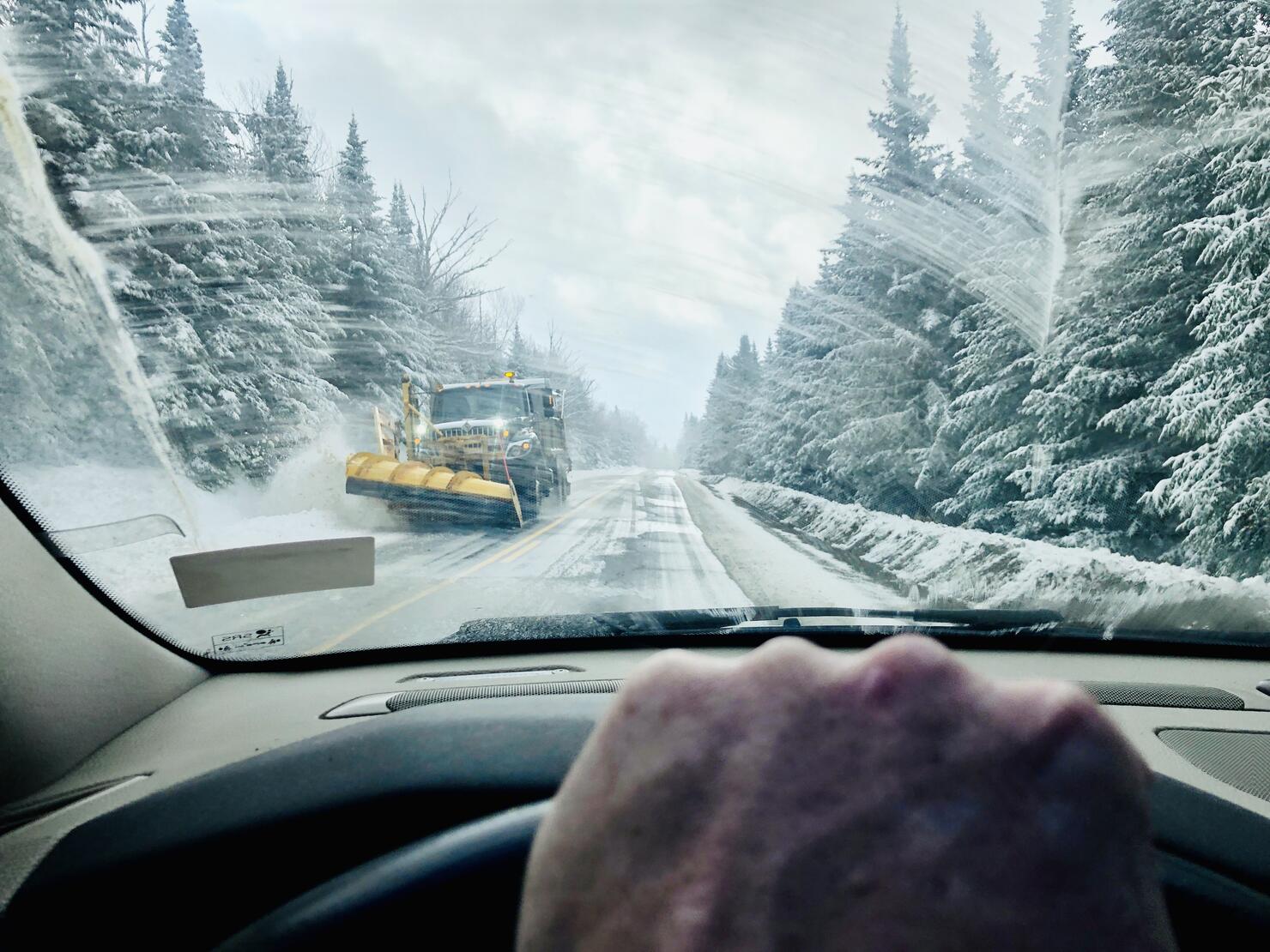 Man driving car during winter in Rangeley, Maine with snowplow coming down road