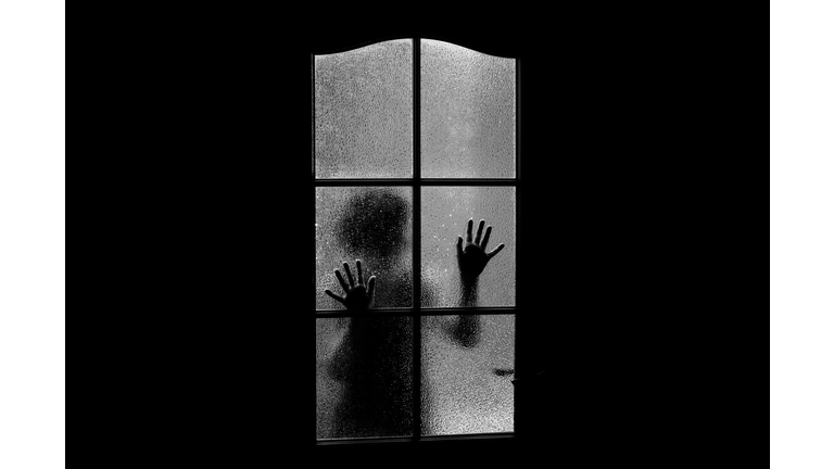 Dark silhouette of girl behind glass. Locked alone in room behind door on Halloween in grayscale. Nightmare of child with aliens, monsters and ghosts. Evil in home in monochrome. Inside haunted house.