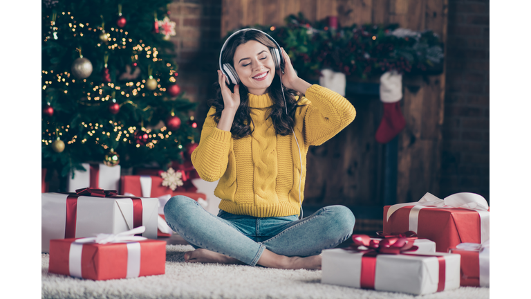 Full length body size photo of rejoicing nice overjoyed girl listening to christmas music rejoicing with new year atmosphere wearing yellow pullover jeans denim sitting on floor