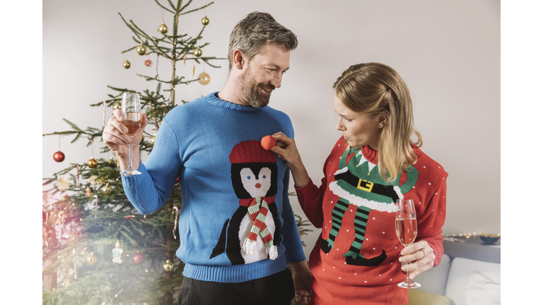 Two people with ugly Christmas sweaters laughing in front of tree