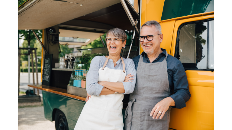 Happy mature couple looking away while standing against food truck