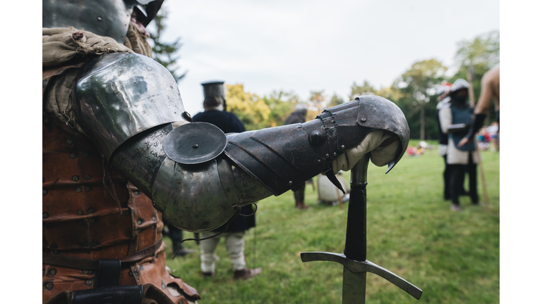 A knight in body armor with a long sword standing at a medieval festival