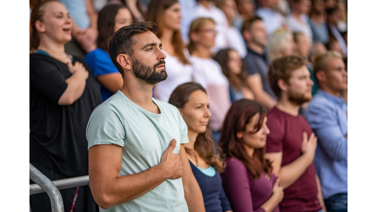 Spectators singing national anthem in stadium