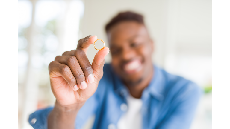 Close up of african man hand holding golden alliance as romatic marriage symbol smiling cheerful