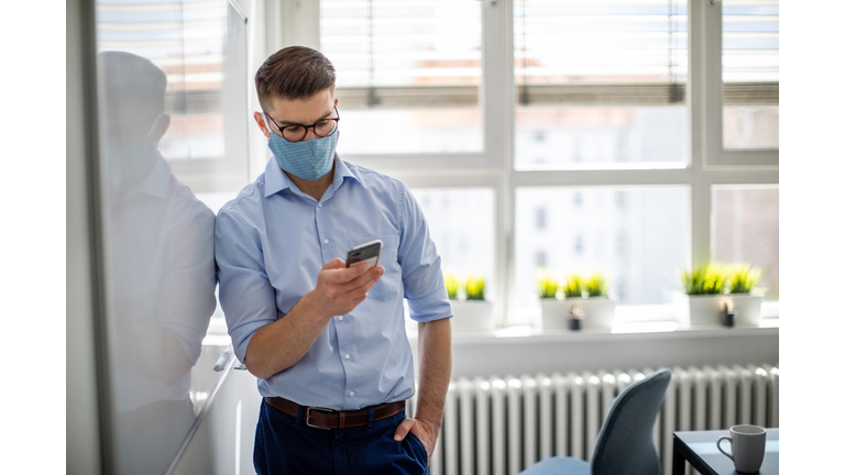 Businessman with face mask in office using mobile phone