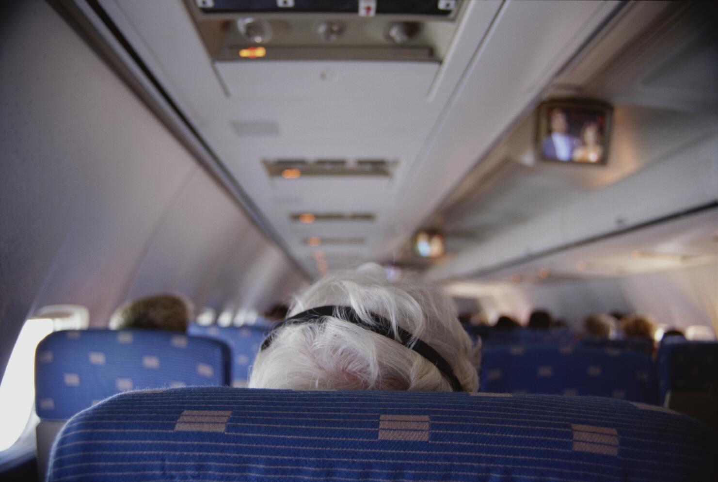 Senior man using headphones on airplane