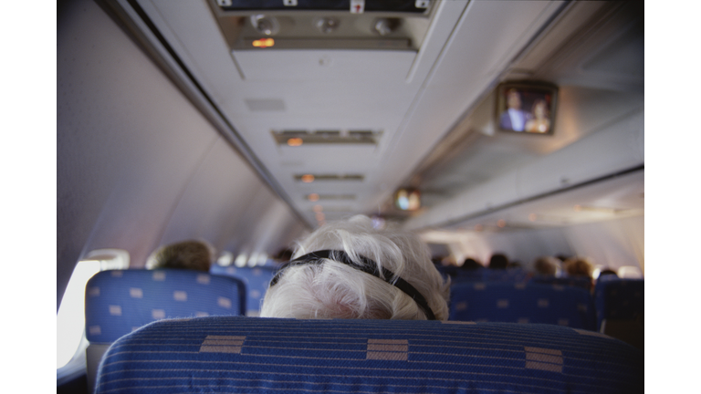 Senior man using headphones on airplane