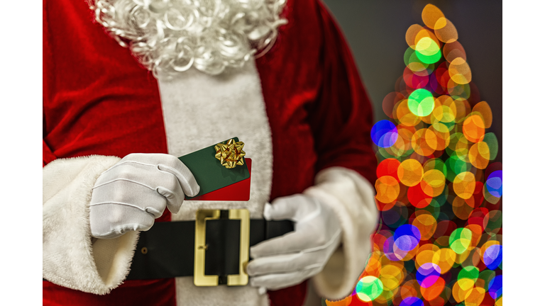 Santa Claus holding a pair of gift cards with a bow and bokeh from Christmas tree in the background