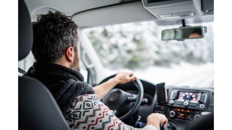 Rear view of mature man driving car on snowy road.