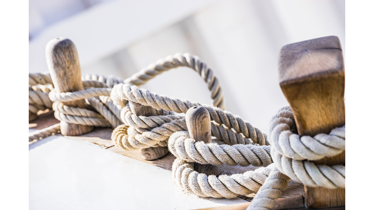 Old sailboat, detail closeup of wooden cleats with nautical moored ropes