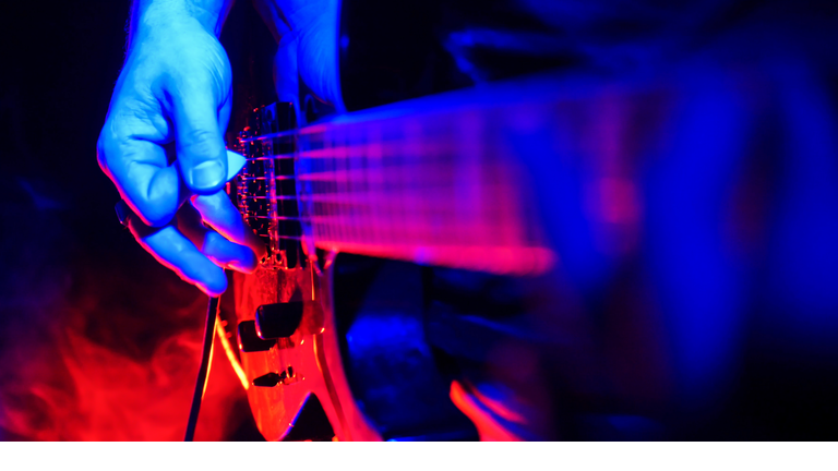 Rock concert. Guitarist plays the guitar. The guitar illuminated with bright neon lights. Focus on hands