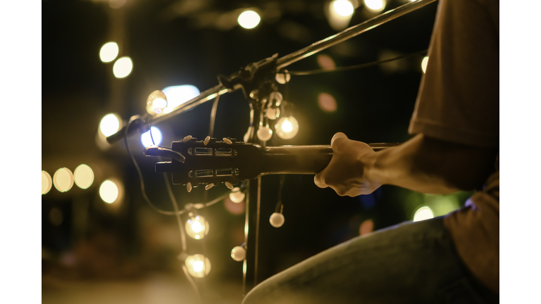 Rear view of the man sitting play acoustic guitar on the outdoor concert with a microphone stand in the front, musical concept.