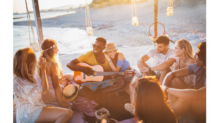 Young friends with guitar having fun at summer beach party