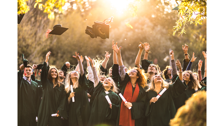 Large group of happy college students celebrating their graduation day outdoors.