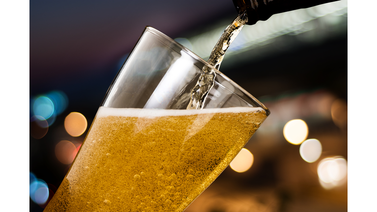 Motion of beer pouring from bottle into glass on bokeh light night background