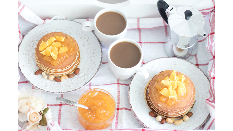 Breakfast for two. American pancakes with orange jam and nuts on vintage plates and 2 white coffee cups. Top view