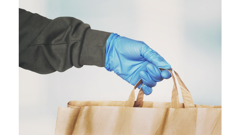 Delivery person hand wearing blue protective glove giving paper bag