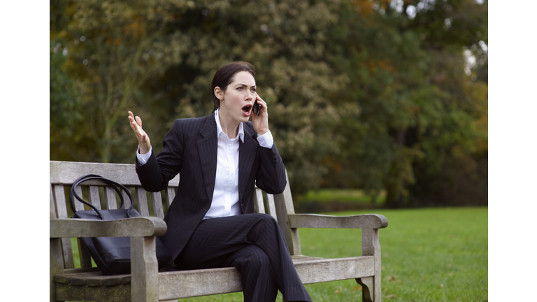 Business woman on park bench using mobile phone.