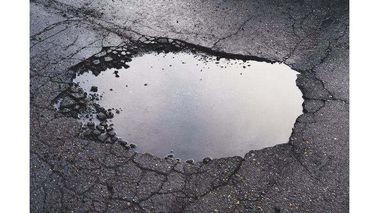 Water filled pothole on urban street with cracks and fracture marks