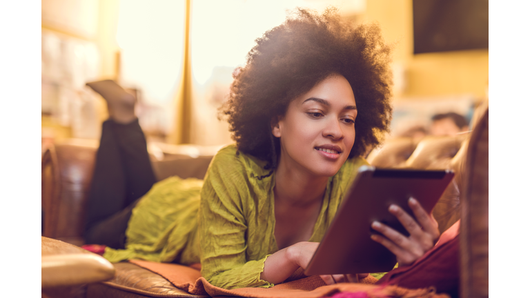 African American woman reading something from e-reader at home.