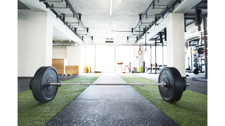 Metal heavy barbell laid on the floor in modern gym.