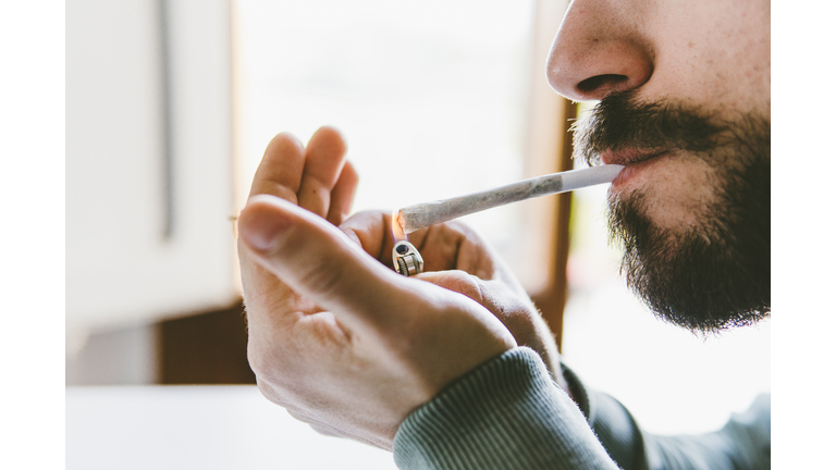Midsection of bearded man igniting marijuana joint with cigarette lighter at home