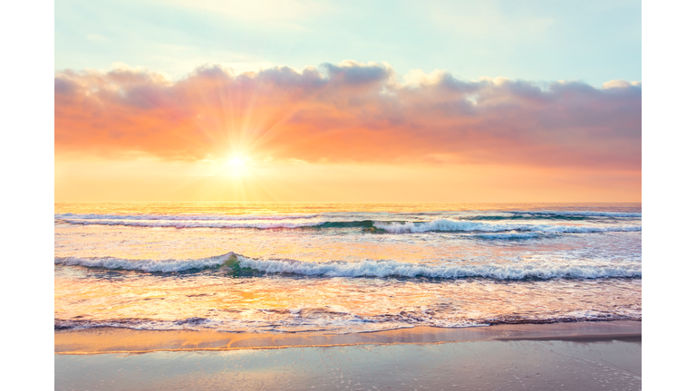 Ocean wave on the beach at sunset time, sun rays.