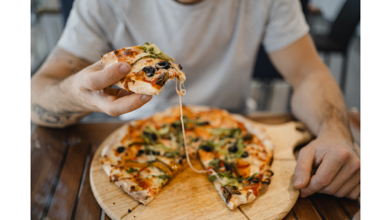 caucasian young man with hat eating a pizza with vegetables on a wooden table