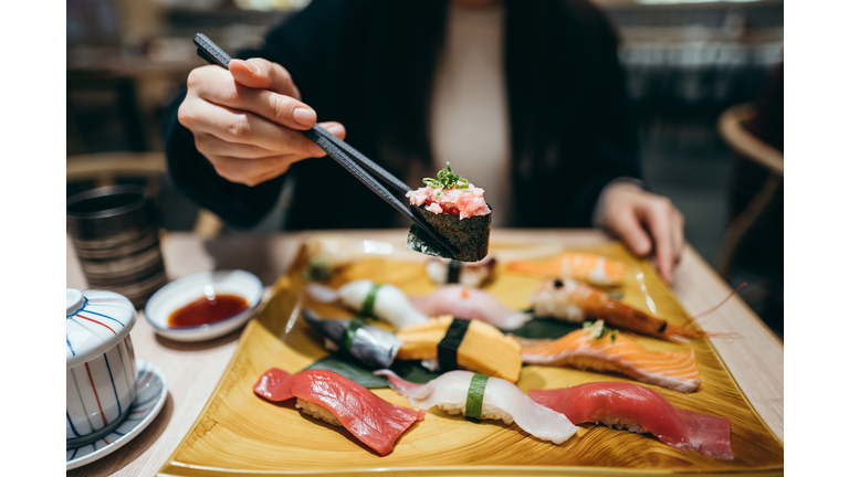 Close up of young Asian woman eating freshly made sushi with side dish and green tea in a Japanese restaurant
