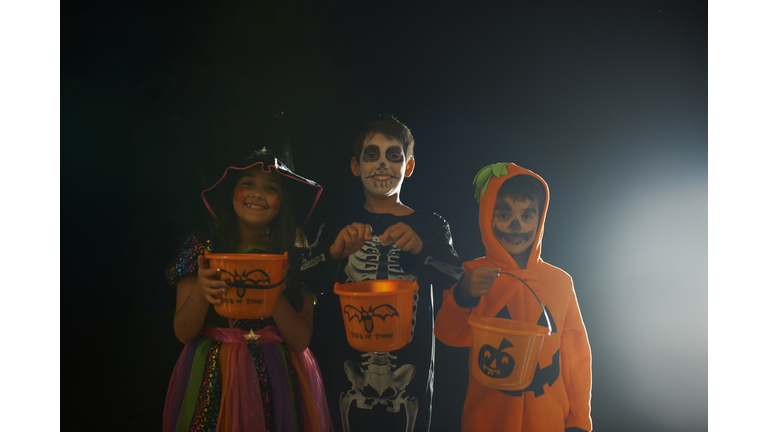 Portrait of brothers and sister wearing halloween costumes holding trick or treat buckets