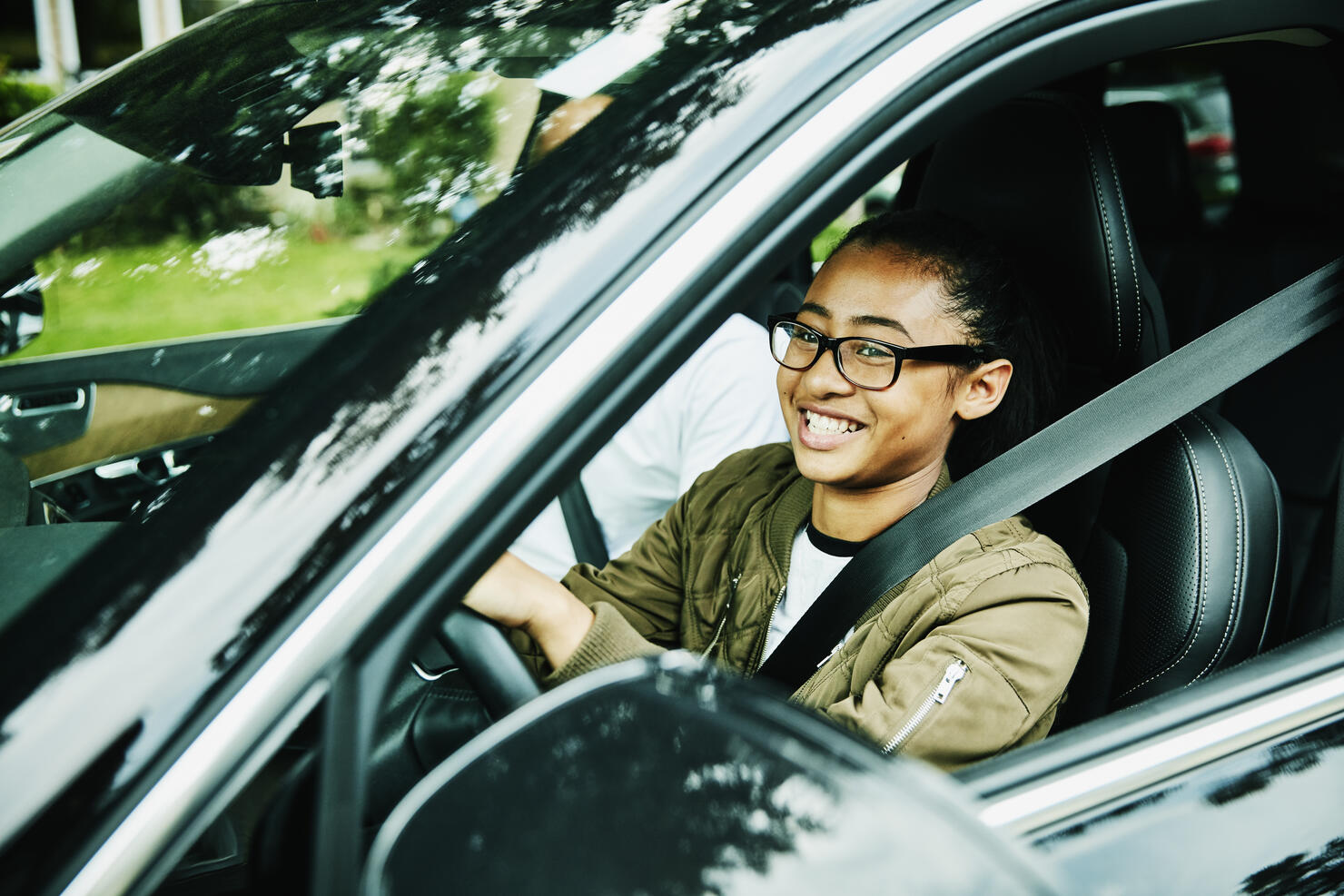 Laughing young woman in drivers seat of car taking driving lesson from father