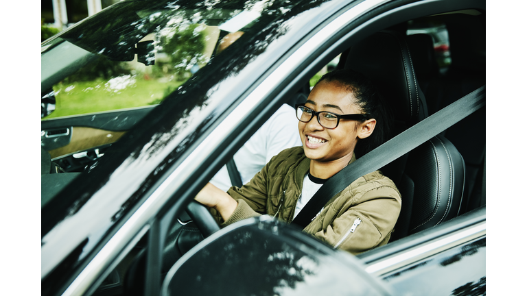 Laughing young woman in drivers seat of car taking driving lesson from father