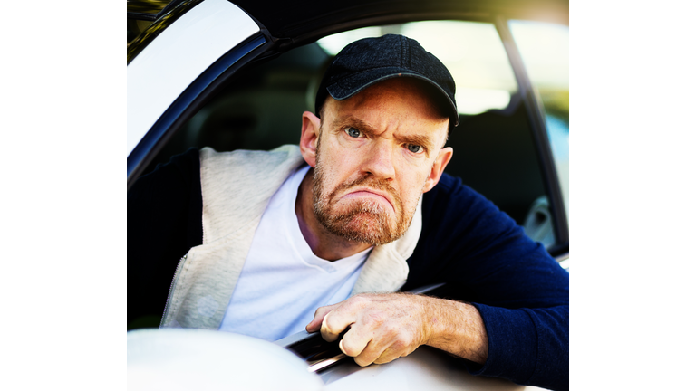 Angry male driver looks through car window, grimacing, fist clenched