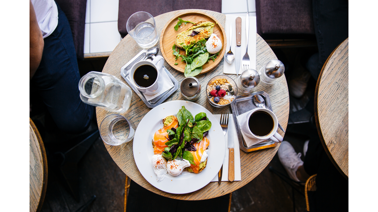 High angle view of brunch with avocado toast, salmon, poached egg and coffee on the table, served in cafe