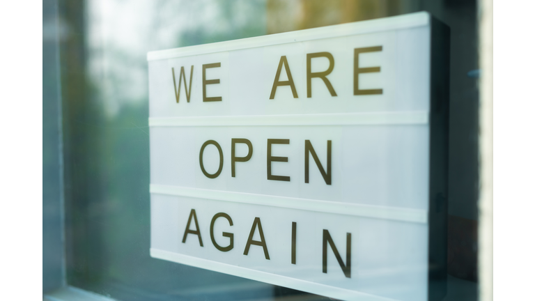 Lightbox with as sign we are open again behind a glass door of the cafe. We're open again after quarantine, video of small business owner. Please wear a face mask and keep your distance to protect