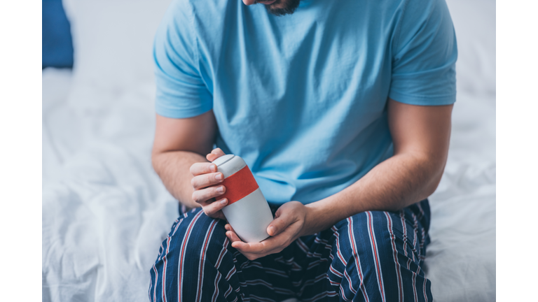 cropped view of man sitting on bed and holding funeral urn