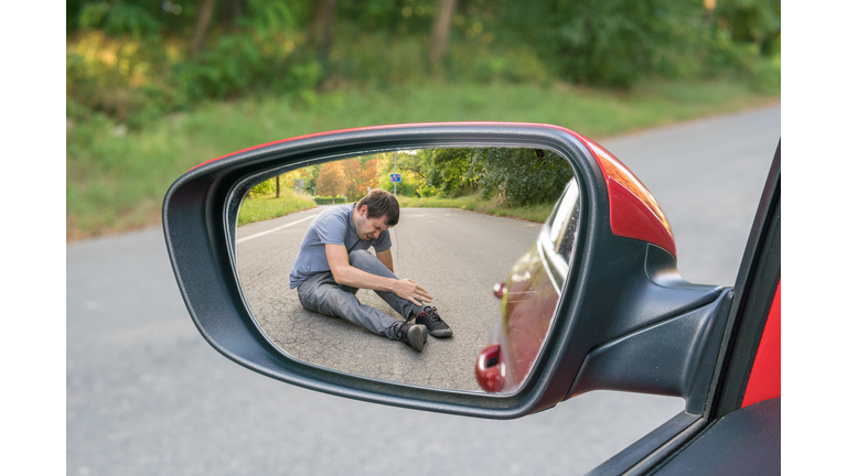 Hit and run concept. View on injured man on road in rear mirror of a car.